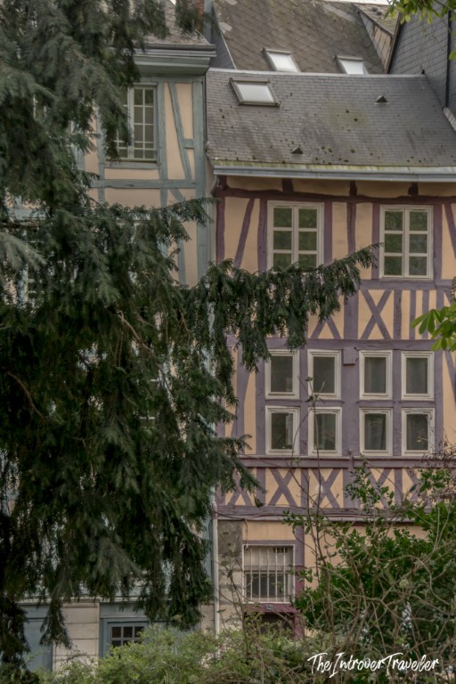 Half-timbered medieval building in Rouen, Normandy, with purple and cream facade framed by trees