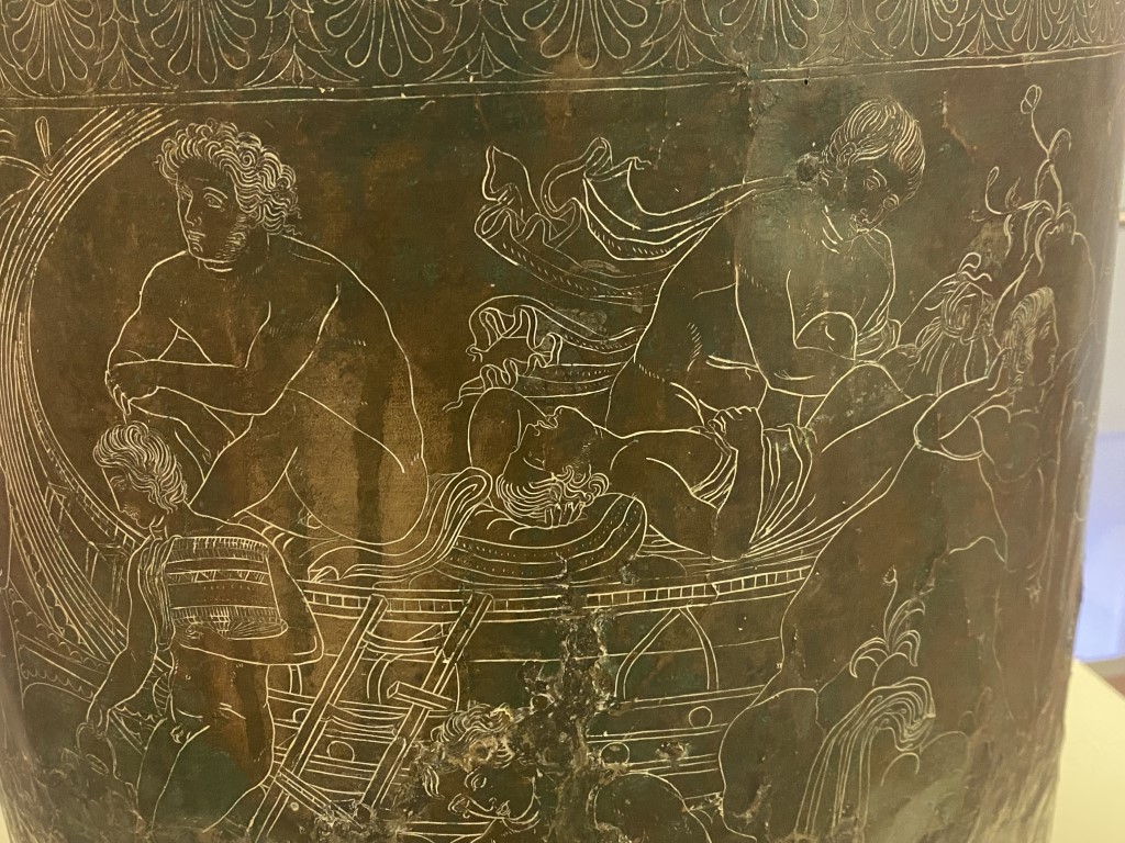 Close-up of engraved bronze vessel at Villa Giulia, showing mythological figures on a boat scene