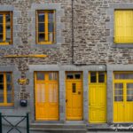 Stone building in Cancale, Brittany, with bright yellow doors and window frames, reflecting the town's coastal charm