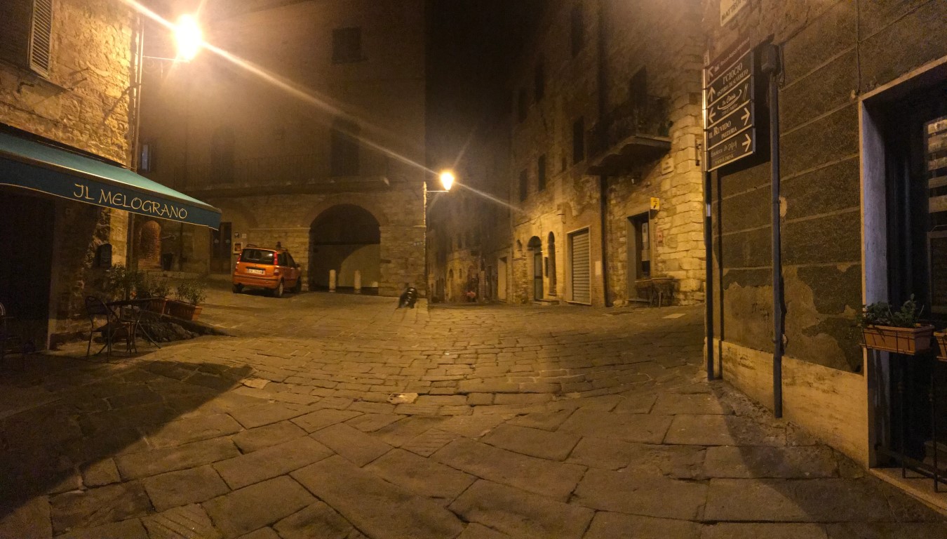 Quiet cobblestone square in Suvereto at night, with Il Melograno restaurant and medieval stone archway