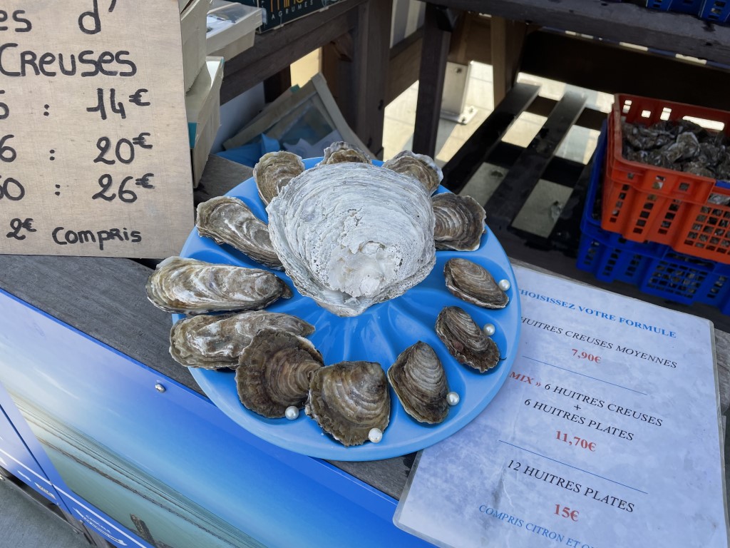 Fresh huitres creuses on display at a Cancale oyster market stall, with French price menus