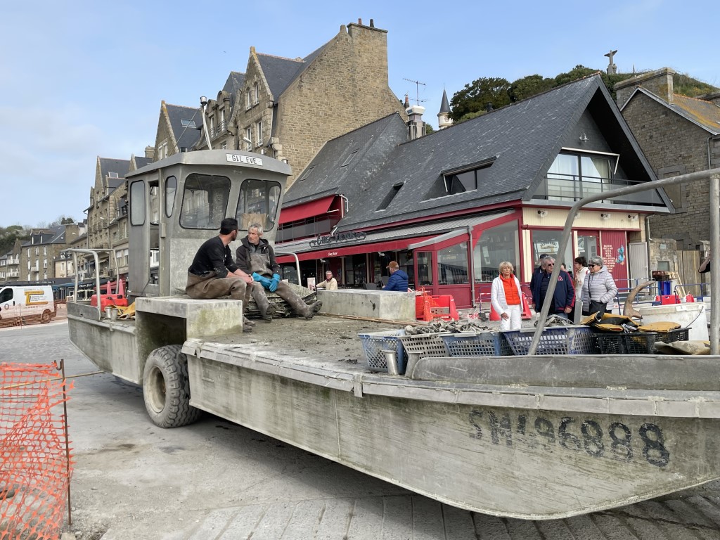 Oyster farmers unloading harvest from a flat-bottomed boat on the Cancale waterfront, Brittany