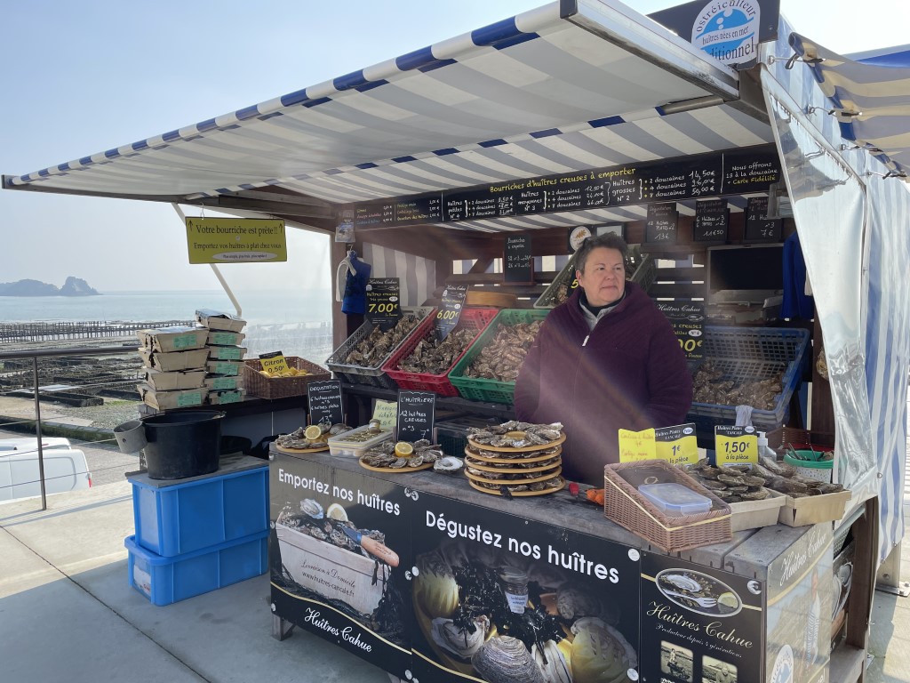 Huitres Cahue oyster stall at Cancale market, with fresh oysters and beds visible behind