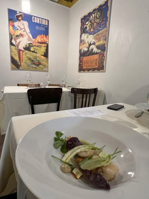 Scallop and vegetable starter at Trattoria da Maro, Bologna, with vintage Italian travel posters on the wall
