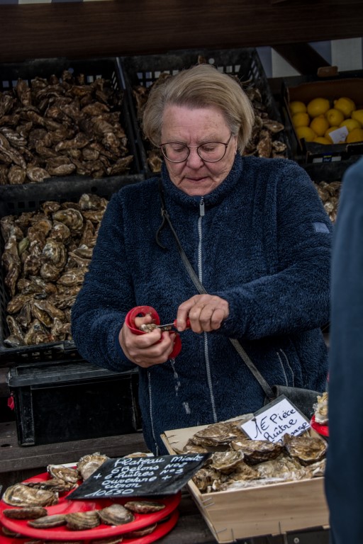 Cancale market vendor shucking fresh Brittany oysters at an outdoor stall in Brittany