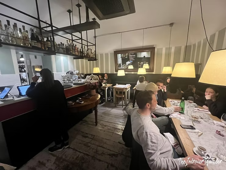 Cozy dining room at Osteria La Quercia Rome, with warm lamps, rustic wood floors, and seated guests