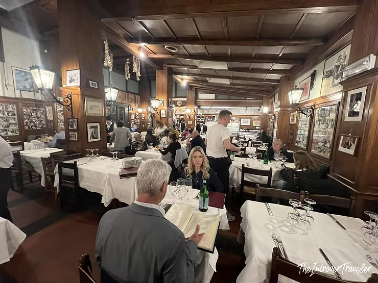 Busy dining room at Checco er Carettiere, Rome, with wood paneling, white tablecloths, and framed photos on walls