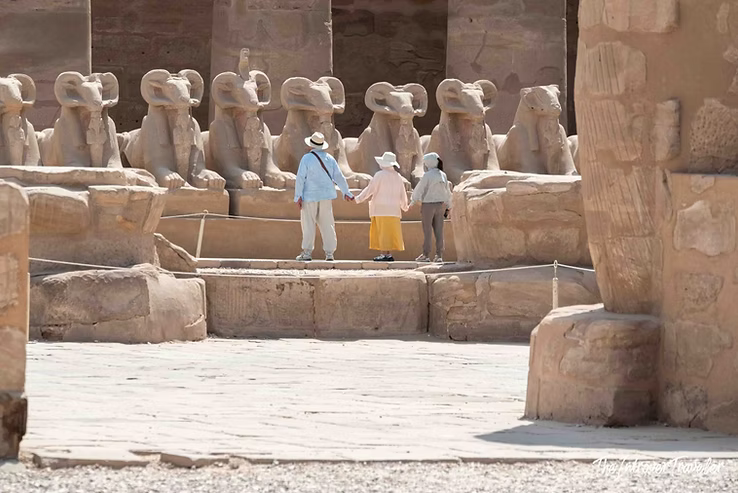 Tourists walking among ram-headed sphinx statues lining the dromos at Karnak Temple Complex, Luxor