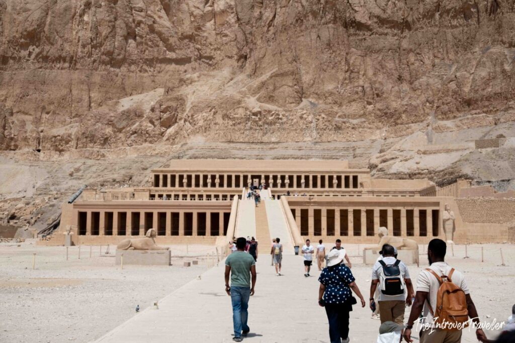 Tourists walking toward the multi-tiered Temple of Hatshepsut, built into the Luxor cliffs at Deir el-Bahari