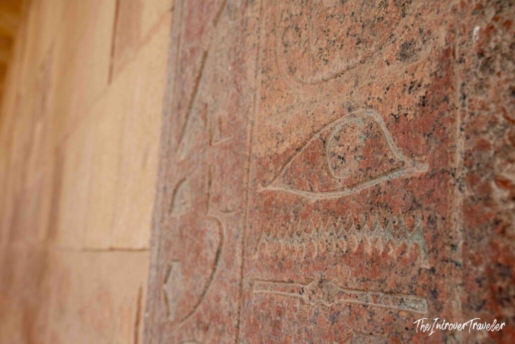 Close-up of ancient Egyptian hieroglyphs carved into red granite at the Temple of Hatshepsut, Luxor