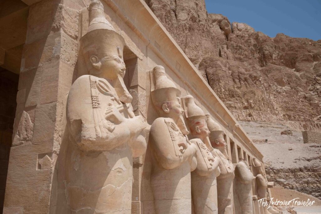 Row of Osiride statues of Hatshepsut lining the upper terrace colonnade, carved into the cliffside at Deir el-Bahari