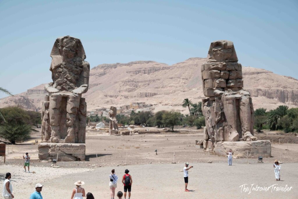 Colossi of Memnon, two massive seated statues near Luxor, with tourists and desert hills behind