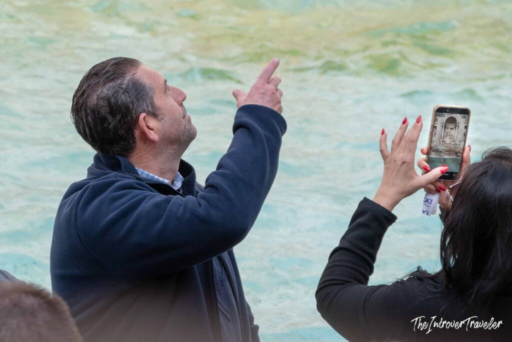 Tourist tossing a coin and visitor filming the Trevi Fountain with a phone, Rome