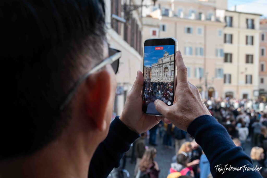 Visitor filming the crowd at the Trevi Fountain on a phone from above, Rome